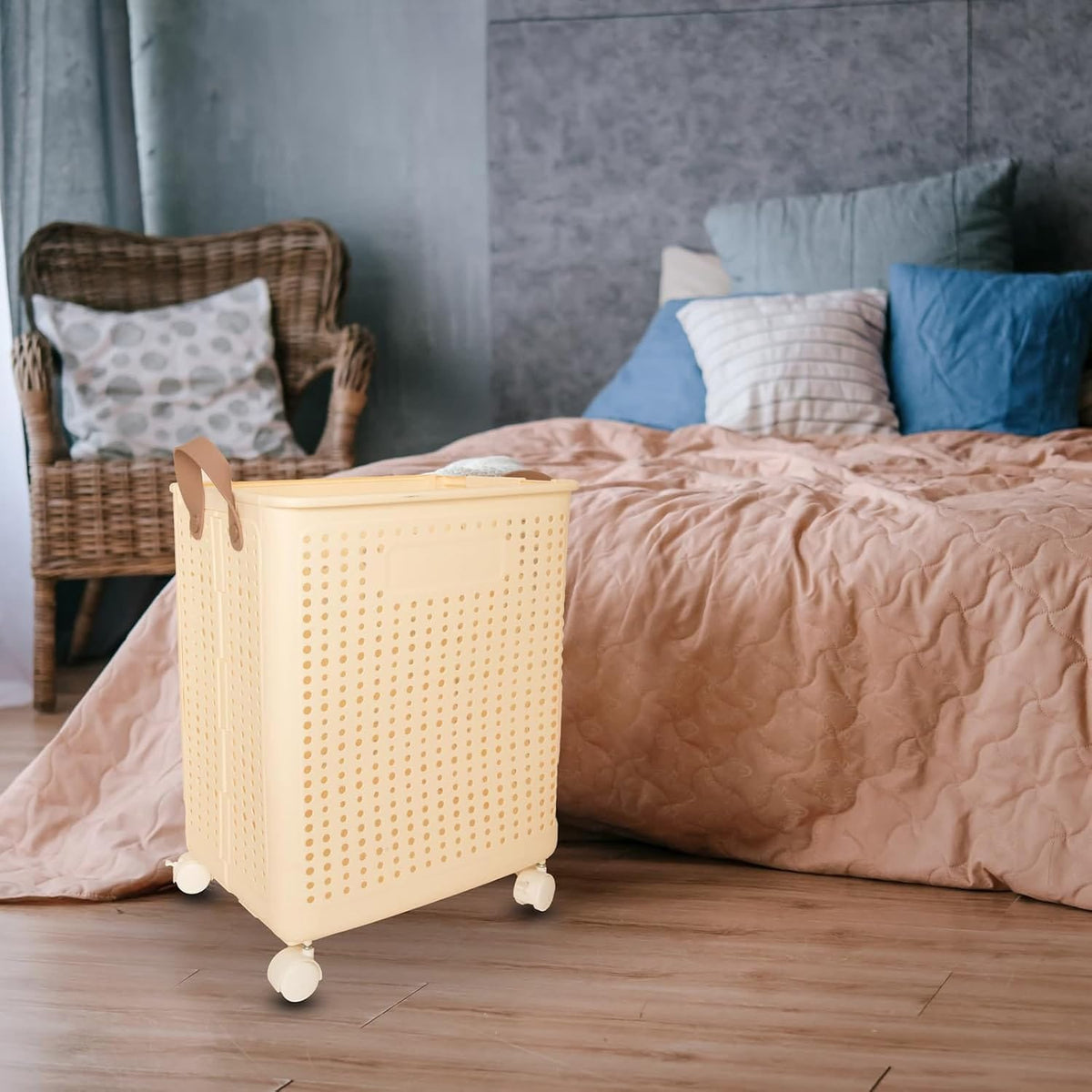 Beiger Wäschekorb mit Lederhenkeln und Rädern in einem Anwendungsbeispiel neben einem Bett