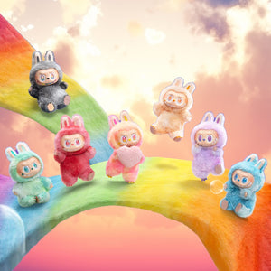 Sechs kleine Plüschtiere in verschiedenen Farben auf einem Regenbogen mit Wolken im Hintergrund