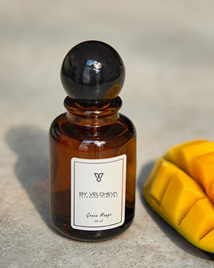 Raumduft Spray in kleiner, braunen Glasflasche mit schwarzem Deckel neben einem geschnittenem StĂĽck Mango
