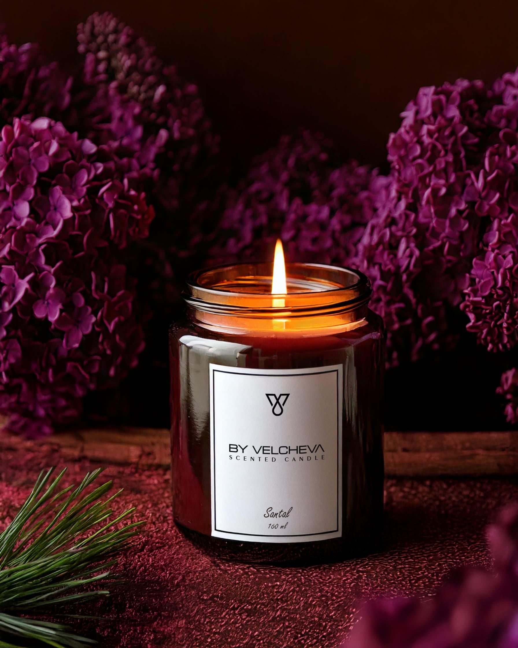 Brennende Duftkerze in einem braunen Glas mit lila Blumen im Hintergrund
