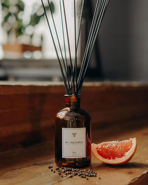 Raumduft mit Holzstäbchen in einem braunen Glas neben Pfeffer und Grapefruit