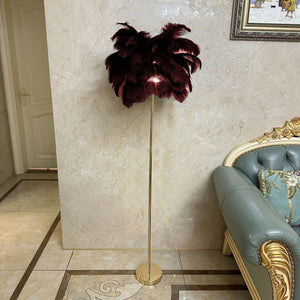 Stehlampe mit roten Straussenfedern und goldenem Ständer neben einem blauen Sofa und beiger Wand
