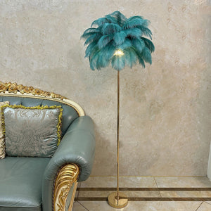 Stehlampe mit blauen Straussenfedern und goldenem Ständer neben einem blauen Sofa und beiger Wand