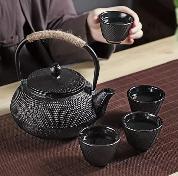 Schwarze Teekanne in asiatischem Stil mit vier dazugehörigen Tassen auf einem Tisch mit rotem Untersetzer
