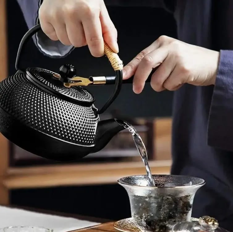 Schwarze, handgehaltene Teekanne in asiatischem Stil mit Deckelhalter in einem Anwendungsbeispiel mit transparenter Tasse