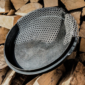 Silberner Ringreiniger in einem Feuertopf mit Holzstapel im Hintergrund