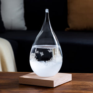 Sturmglas in Form eines Wassertropfens mit Holzständer mit Sofa im Hintergrund