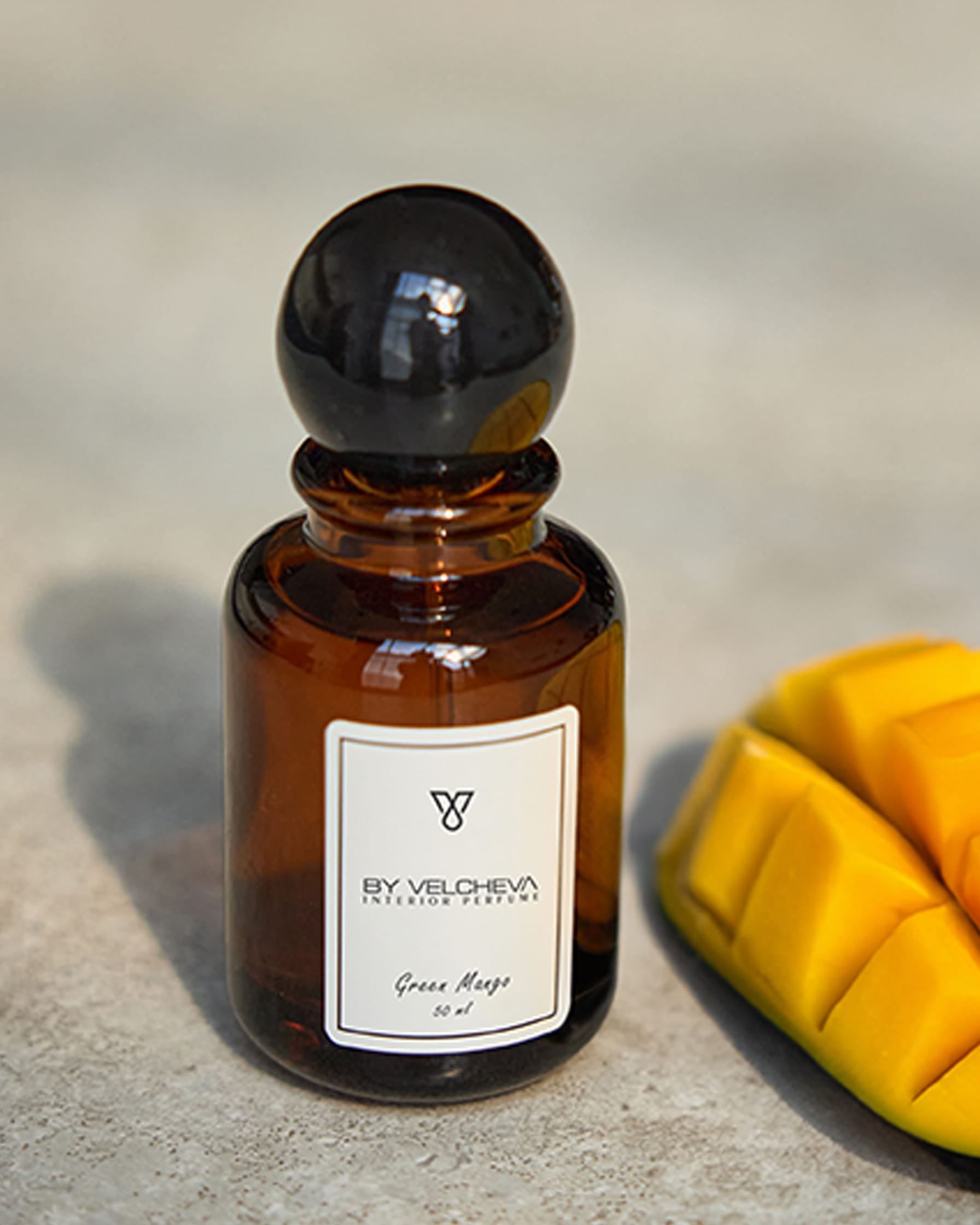 Raumduft Spray in kleiner, braunen Glasflasche mit schwarzem Deckel neben einem geschnittenem Stück Mango