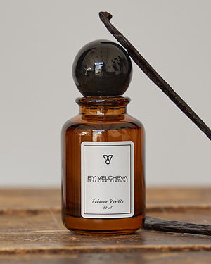 Raumduft Spray in kleiner, braunen Glasflasche mit schwarzem Deckel neben einer Vanillestange
