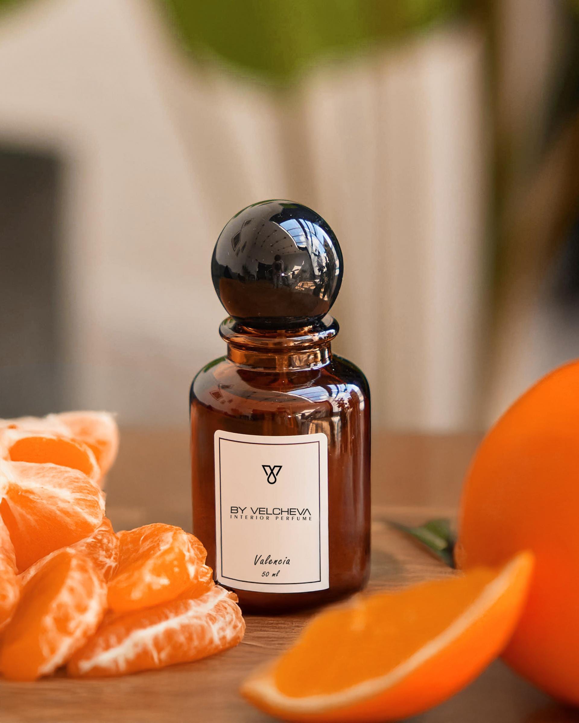 Raumduft Spray in kleiner, braunen Glasflasche mit schwarzem Deckel neben geschnittener Orange