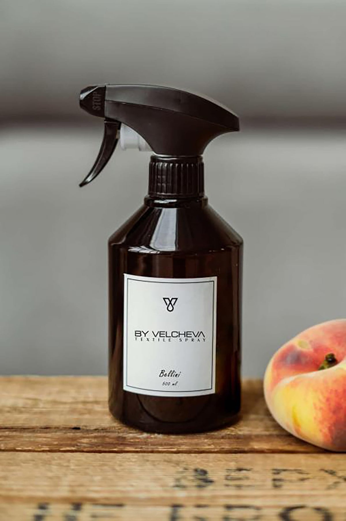 Braune Sprühflasche mit weissem Etikett neben Pfirsich