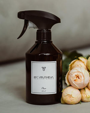 Braune Sprühflasche mit weissem Etikett neben Rosen